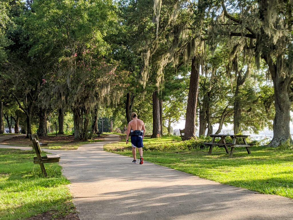A shirtless man jogs along a tree-lined path.