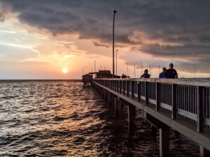 A long pier extends into the Gulf of Mexico at sunset.