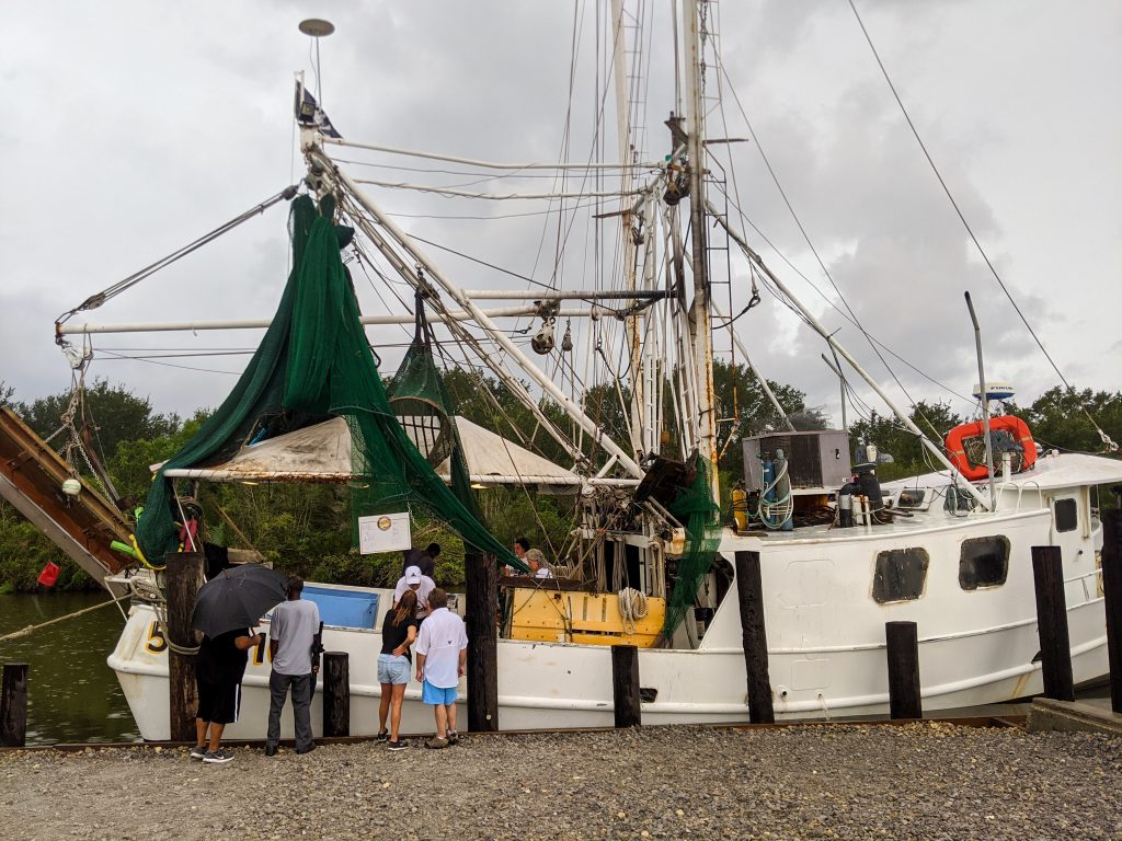 People line up at a white shrimp boat docked under a stormy sky on a day trip to St. Bernard Parish