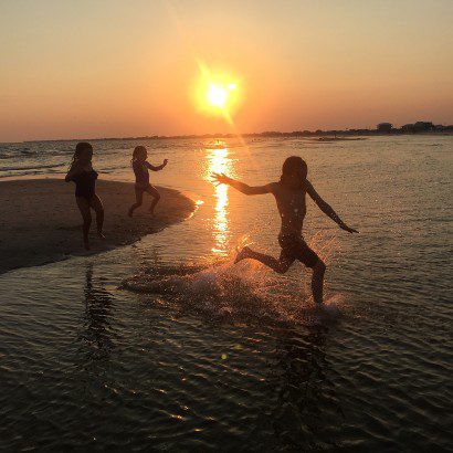 Three children run along a beach at sunset.